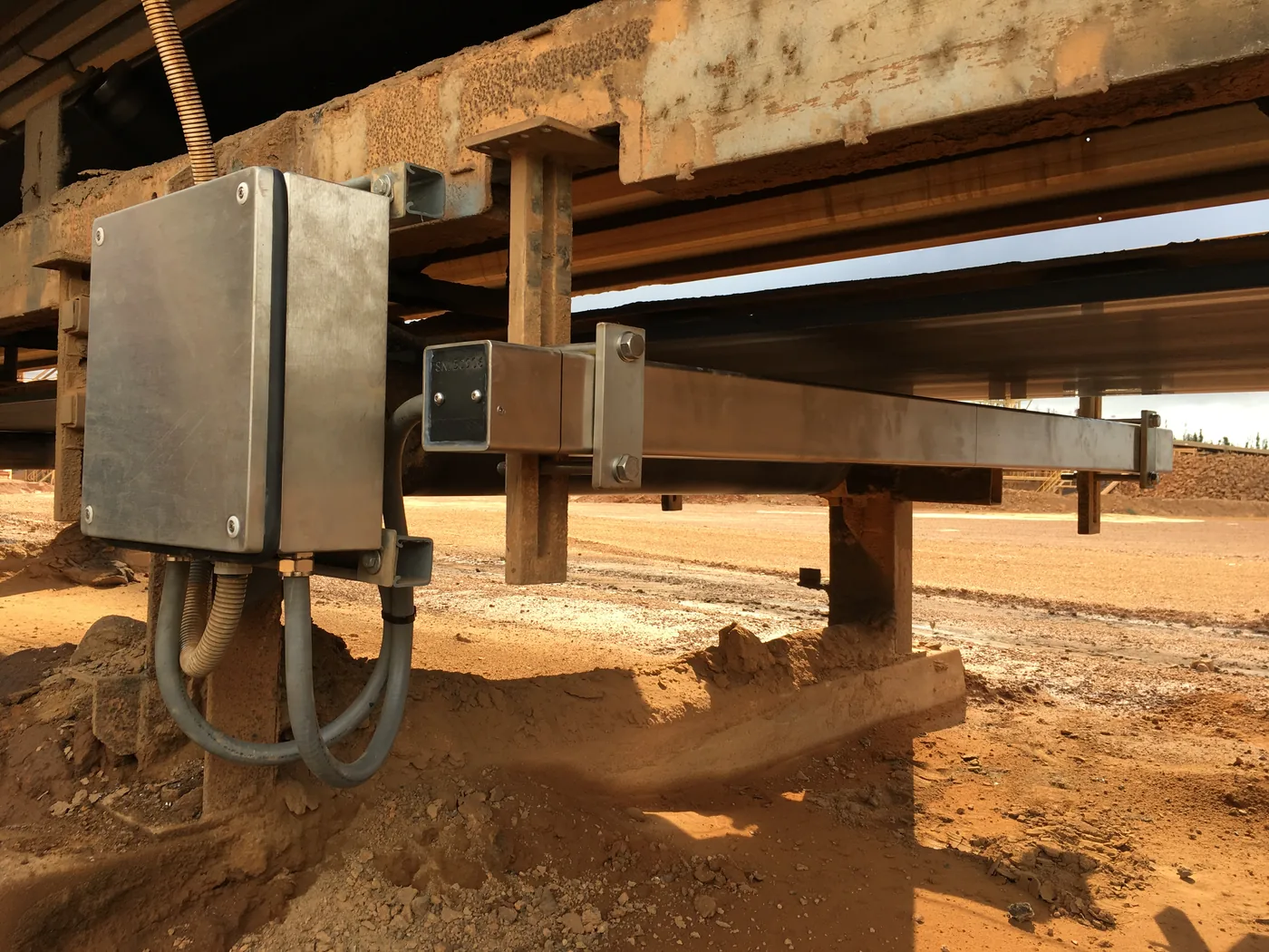 Stainless steel termination enclosure mounted on a conveyor stringer with conduit runs, alongside the scanner.